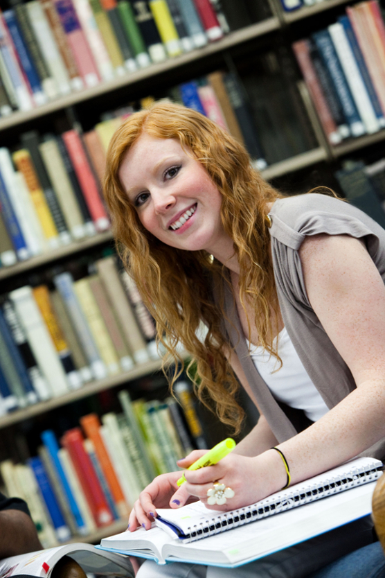 girl smiling and writing in library