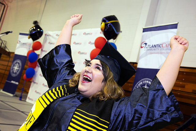 Student in cap and gown with arms raised in celebration