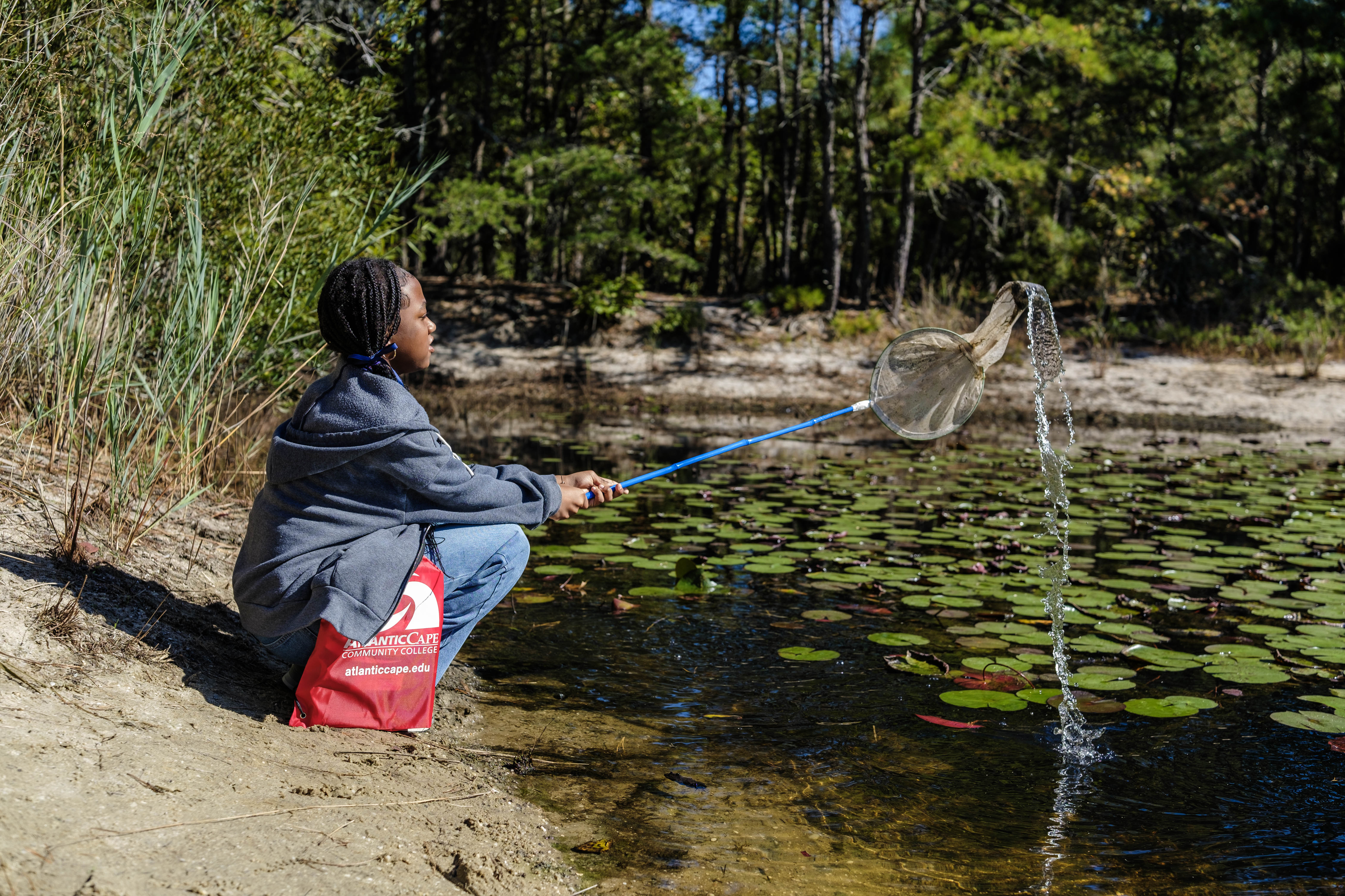 Student looks for aquatic life in a pond behind the campus